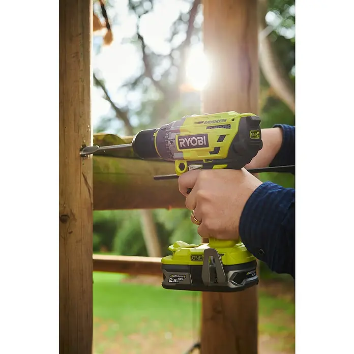 Ryobi ONE+ Akku-Schlagbohrschrauber R18PD7-252S - 18 V, 2 Akkus, 5 Ah, 85 Nm - Nahaufnahme eines gelben Ryobi Akku-Bohrers, der in einen Holzpfosten bohrt, mit Fokus auf das Werkzeug und seine Verwendung im Freien.