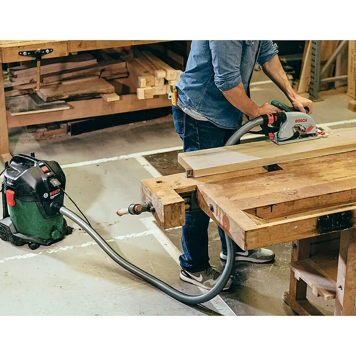 Bosch Elektro-Staubsauger EasyVac 3 - 700 W, Behältervolumen: 2,1 l - Ein Handwerker benutzt eine Bosch Kreissäge mit Staubabsaugung an einem Holztisch in seiner Werkstatt.