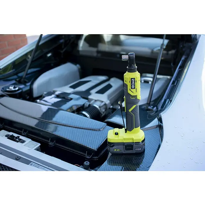 Ryobi ONE+ Akku-Ratschenschrauber R18RW2-0 - 18 V, Ohne Akku, ¼″ - Ryobi Akku-Ratschenschlüssel vor einem geöffneten Motorraum. Ideal für Reparaturen und Wartungsarbeiten am Auto.