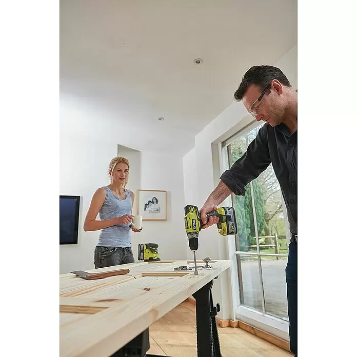 Ryobi ONE+ Akku-Schlagbohrschrauber R18PD5-0 - 18 V, Ohne Akku, 50 Nm - Mann bohrt ein Loch in ein helles Holzbrett mit einem gelb-schwarzen Ryobi Bohrer.