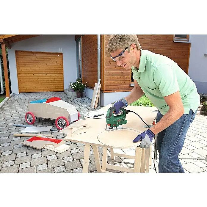 Bosch Elektro-Stichsäge PST 700 E - 500 /min - 3.100 /min, 70 mm, 500 W - Mann sägt mit einer Stichsäge Kreise aus einer Holzplatte. Er trägt Schutzbrille und Handschuhe für die Sicherheit.