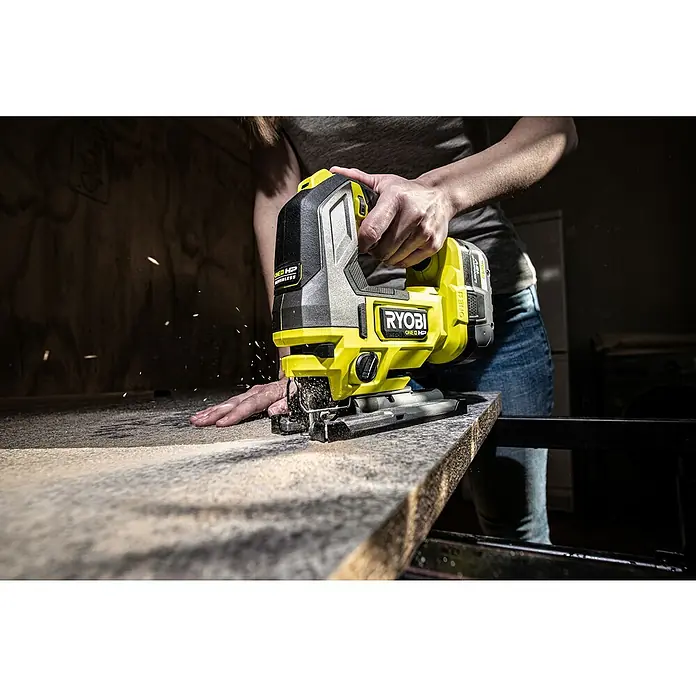 Ryobi ONE+HP Akku-Stichsäge RJS18X-0 Performance - 18 V, Ohne Akku, Leerlaufhubzahl: 800 /min - 3.400 /min - Nahaufnahme einer Person, die mit einer gelben und grauen RYOBI Stichsäge ein Stück Holz sägt, wobei Sägespäne umherfliegen.