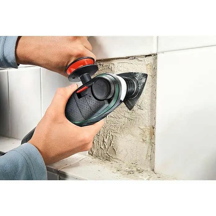 Bosch Elektro-Multifunktionswerkzeug PMF 350 CES - 350 W, STARLOCK-System - Ein Bediener verwendet ein Bosch Multifunktionswerkzeug, um Fugenmasse zwischen Fliesen zu entfernen. Das Werkzeug wird mit beiden Händen geführt.