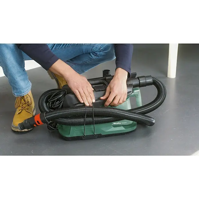 Bosch Elektro-Staubsauger EasyVac 3 - 700 W, Behältervolumen: 2,1 l - Eine Person verstaut den Schlauch und das Kabel eines grünen Nass-Trockensaugers der Marke Microfilter System.