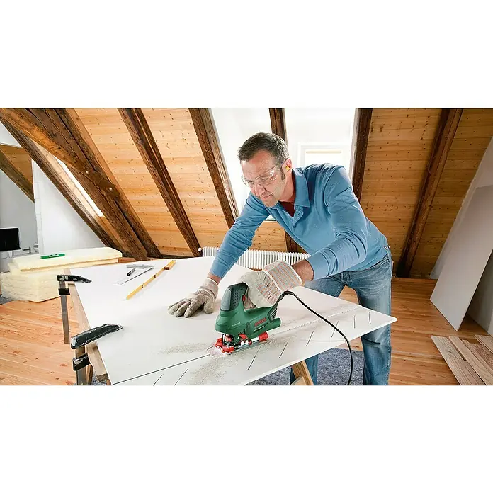 Bosch Elektro-Stichsäge PST 650 - 3.100 /min, 65 mm - Mann benutzt eine Bosch Stichsäge, um ein Werkstück in einem Dachgeschoss zu schneiden. Er trägt dabei eine Schutzbrille für die Sicherheit.