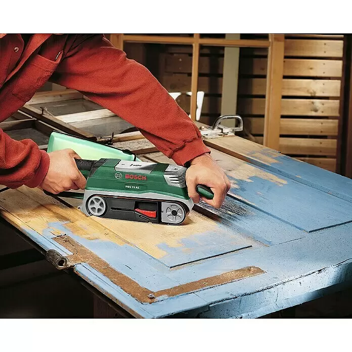 Bosch Elektro-Bandschleifmaschine PBS 75 AE - 750 W - Grüner und schwarzer Bosch PBS 75 AE Bandschleifer entfernt blaue Farbe von einer Holztür.