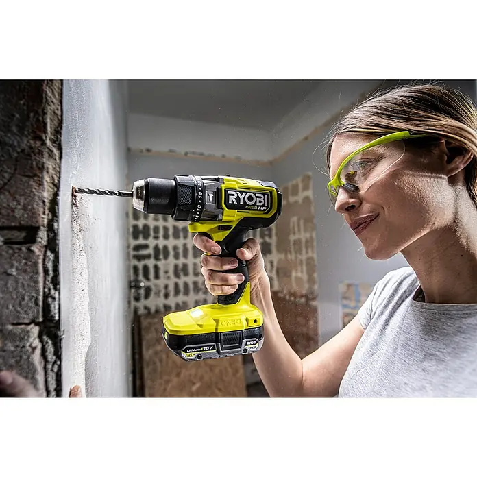 Ryobi ONE+HP Akku-Schlagbohrschrauber RPD18X-0 - 18 V, Ohne Akku, 95 Nm - Frau bohrt mit einem gelben Ryobi ONE+ HP Akku-Bohrschrauber in eine Wand und trägt dabei eine Schutzbrille.