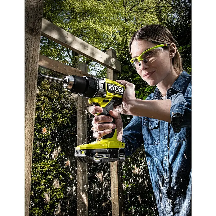 Ryobi ONE+HP Akku-Schlagbohrschrauber RPD18X-0 - 18 V, Ohne Akku, 95 Nm - Eine Frau bohrt mit einem Ryobi ONE+ HP Akku-Bohrschrauber ein Loch in einen Holzzaun. Schutzbrille wird getragen.