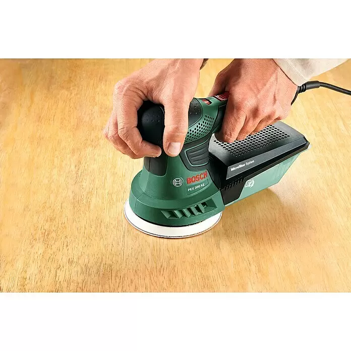 Bosch Elektro-Exzenterschleifer PEX 300 AE - 270 W, Durchmesser Schleifteller: 125 mm - Hände bedienen einen grün-schwarzen Bosch PEX 300 AE Exzenterschleifer auf Holz, mit Microfilter System.