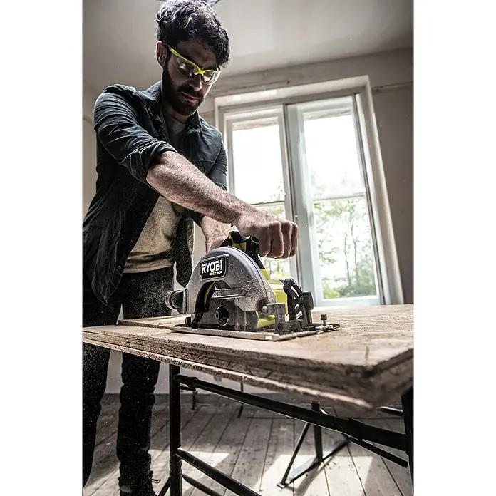 Ryobi ONE+HP Akku-Handkreissäge RCS18X-0 Performance - 18 V, Ohne Akku, 4.500 U/min - Ein Mann benutzt eine Ryobi Kreissäge, um ein Stück Holz zu schneiden, mit Schutzbrille für die Sicherheit.