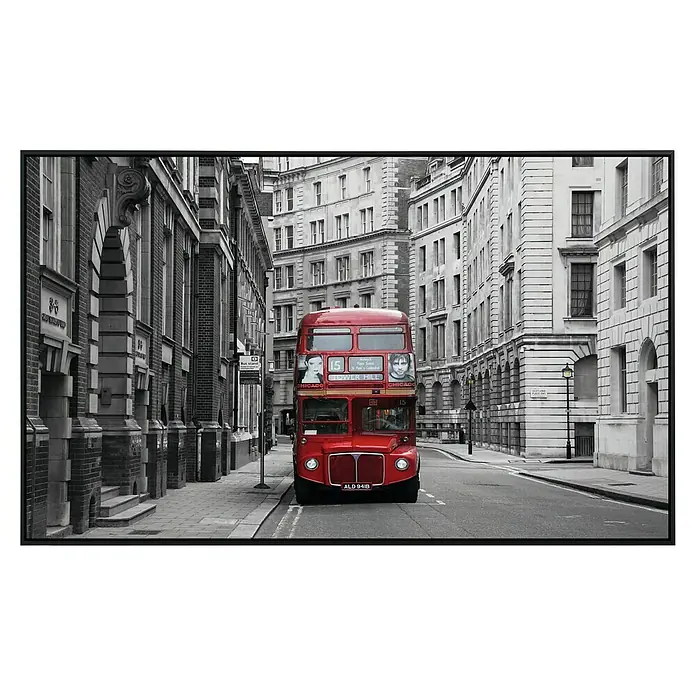 Papermoon Infrarot-Bildheizkörper London - 120 x 60 cm, 1.200 W - Ein roter Doppeldeckerbus fährt auf einer Straße, umgeben von hohen Gebäuden in Schwarzweiß. Der Bus sticht durch seine Farbe hervor.