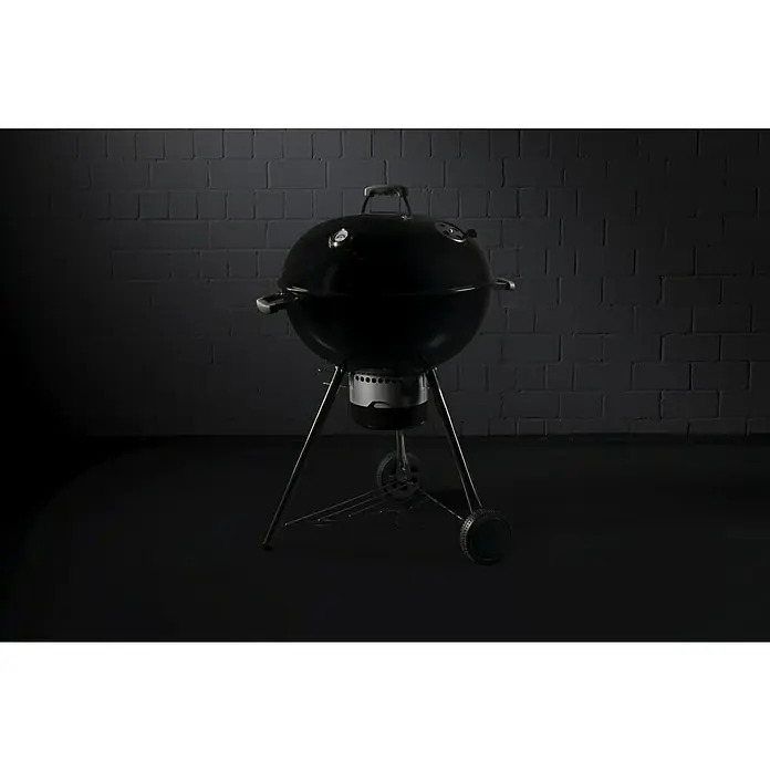 Kingstone Kugelgrill Bullet 66Durchmesser Grillfläche: 66 cm, Schwarz - Schwarzer Kugelgrill vor dunklem Backsteinhintergrund. Das Grillgerät ist mit einem Deckel, Griff und einem Untergestell mit Rädern ausgestattet.
