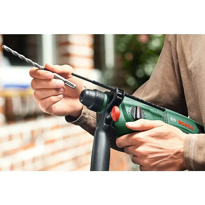 Bosch Kombihammer PBH 2200 RE - 570 W, 1,8 J, SDS-Plus-Aufnahme - Ein Mann wechselt den Bohrer an einer grünen Bosch-Bohrmaschine. Der Bohrer ist silberfarben und spiralförmig.
