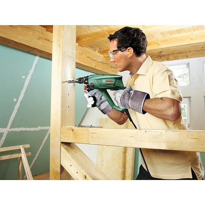 Bosch Bohrhammer PBH 2500 SRE - 600 W, 1,9 J, SDS-Plus-Aufnahme - Ein Mann bohrt mit einer grünen Bosch Schlagbohrmaschine PBH 2100 SRE ein Loch in ein Holzbrett.