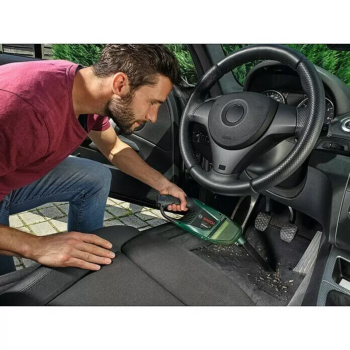 Bosch Power for All 12V Akku-Handstaubsauger EasyVac 12 - 12 V, 1 Akku, 2 Ah - Mann reinigt mit einem grün-schwarzen Bosch Handstaubsauger das Innere eines Autos von Schmutz.