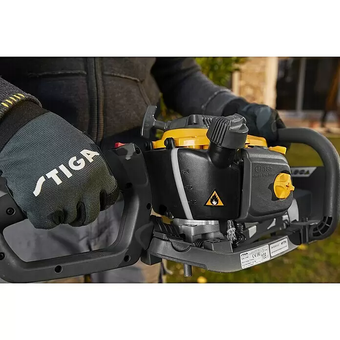 Stiga Benzin-Heckenschere HT 525 - 0,65 kW, Schnittlänge: 46 cm, Max. Aststärke: 27 mm - Eine Person mit STIGA Handschuhen hält eine schwarz-gelbe Benzin-Heckenschere.