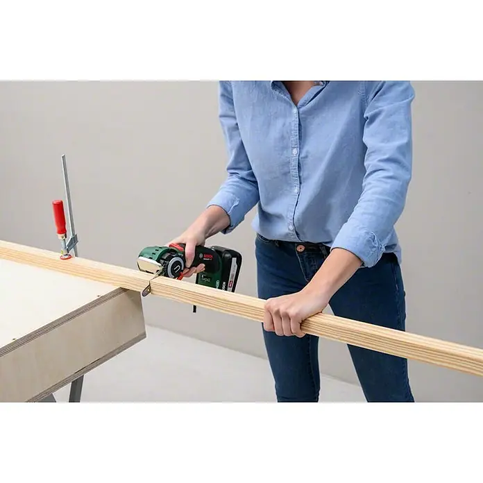 Bosch Power for All 18V NanoBlade-Säge AdvancedCut 18 - Leerlaufdrehzahl: 7.000 U/min, 18 V, 1 Akku - Eine Person benutzt ein Multifunktionswerkzeug von Bosch, um ein Stück Holz zu bearbeiten, das mit einer Klemme an einem Tisch befestigt ist.