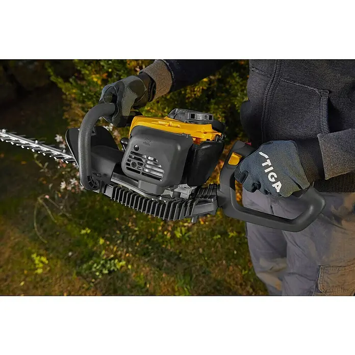 Stiga Benzin-Heckenschere HT 525 - 0,65 kW, Schnittlänge: 46 cm, Max. Aststärke: 27 mm - Eine gelb-schwarze Stiga-Heckenschere wird von einer Person gehalten, die graue Handschuhe und Kleidung trägt.