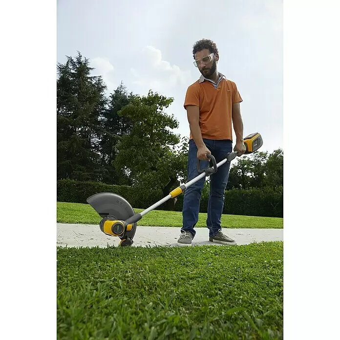 Stiga 500er Serie Akku-Rasentrimmer GT 500e - Set - 48 V, 2 Ah, Li-Ionen, 1 Akku, Schnittbreite Faden: 30 cm - Mann mit Schutzbrille trimmt Grasränder mit gelb-schwarzem Rasentrimmer entlang eines Weges.
