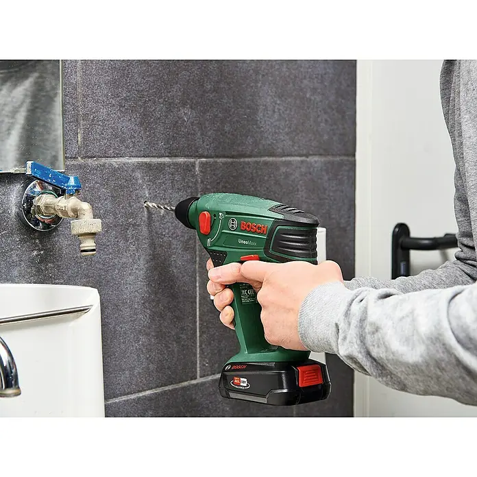 Bosch Power for All 18V Akku-Bohrhammer Uneo Maxx - 18 V, 2 Akkus, 0,6 J - Nahaufnahme einer Person, die mit einem grünen Bosch UneoMaxx Akku-Bohrhammer in eine geflieste Wand bohrt.