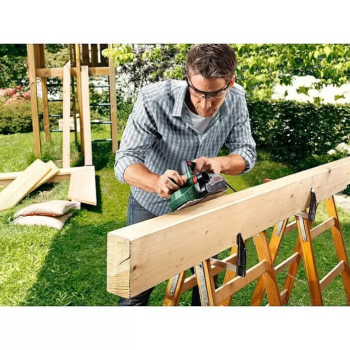 Bosch Elektrohobel PHO 2000 - 680 W, Hobeltiefe: 0 mm - 2 mm - Mann hobelt einen Holzbalken mit einem grünen Bosch Elektrohobel im Freien.