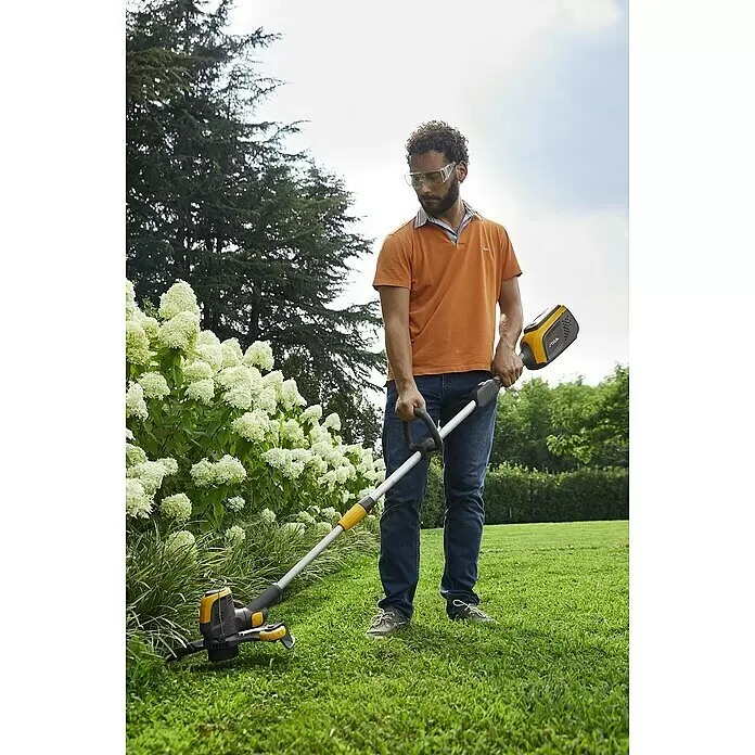 Stiga 500er Serie Akku-Rasentrimmer GT 500e - 48 V, 2 Ah, Li-Ionen, Ohne Akku, Schnittbreite Faden: 30 cm - Mann mit Schutzbrille trimmt Gras im Garten mit einem gelb-schwarzen Rasentrimmer.