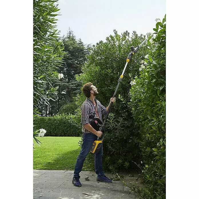 Stiga 500er Serie Akku-Multitool MT 500e - 48 V, Ohne Akku - Mann trimmt eine hohe Hecke im Garten mit einem gelb-schwarzen Akku-Stielheckenschneider.