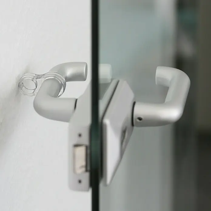 Wandtürstopper - Kunststoff, 4 Stk., Transparent - Detailaufnahme eines silbernen Türgriffs an einer Glastür, montiert an einer weißen Wand, mit Fokus auf Design und Funktionalität.