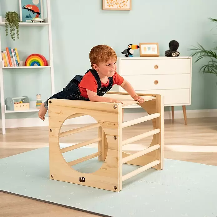 TP Toys Klettergerüst Active Tots Cube - 62 x 60 x 52 cm, Holz, Natur - Ein lächelndes Kleinkind mit roten Haaren kriecht auf einem Kletterwürfel aus Naturholz, einer Montessori-inspirierten Spielstruktur.