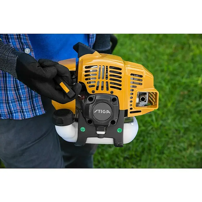 Stiga Benzin-Motorsense GT 330 A - 700 W, Schnittbreite Faden: 38 cm - Nahaufnahme eines gelben Stiga-Motorsägenkopfes, der von einer Person mit Handschuhen gehalten wird, vor einem grünen Rasen.