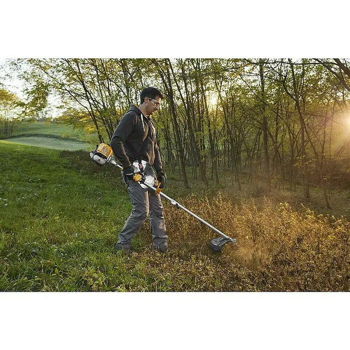 Stiga Benzin-Motorsense BC 330 A - 700 W, Schnittbreite Faden: 43 cm, Schnittbreite Messer: 25,5 cm - Ein Mann benutzt einen STIGA Freischneider im Freien, um hohes Gras zu trimmen. Das Gerät ist gelb und silber.