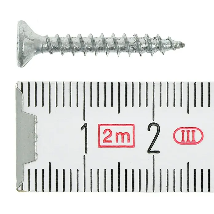 Profi Depot Tornillo para madera - Ø x L: 3,5 x 25 mm, 200 ud., Zincado, Ranura en forma de cruz Pozidriv - Primer plano de un tornillo colocado junto a una cinta métrica. El tornillo es plateado y tiene una rosca.