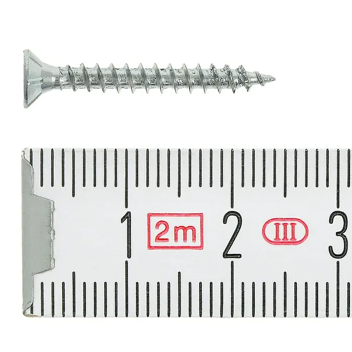 Profi Depot Tornillo para madera - Ø x L: 3 x 25 mm, 1.000 ud., Zincado, Ranura en forma de cruz Pozidriv - Primer plano de un tornillo plateado junto a una regla. El tornillo tiene un extremo plano y se coloca sobre una superficie blanca.