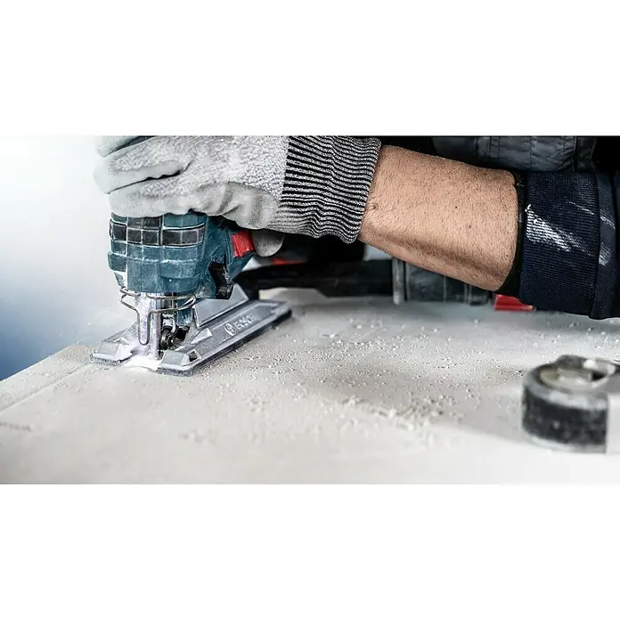 Bosch Expert Säbelsägeblatt Fiber Plaster T141 HM - Länge: 100 mm - Nahaufnahme einer Stichsäge von Bosch in Aktion, die durch ein weißes Material schneidet. Staubpartikel und ein Arbeiter mit Schutzhandschuhen sind sichtbar.