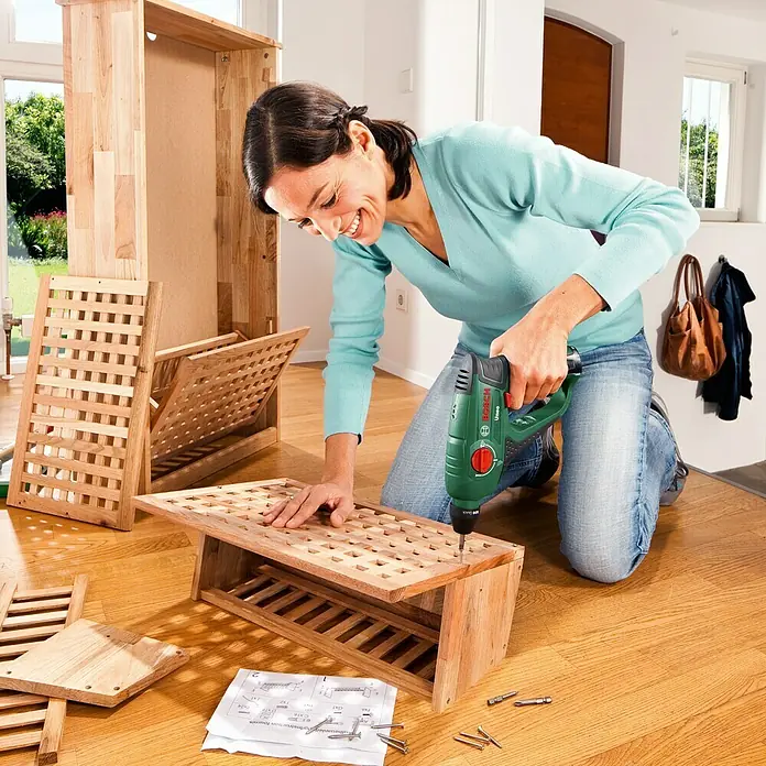 Bosch Power for All 12V Martillo perforador de batería Uneo - 12 V, 1 batería, 2 Ah, 0,5 J - Una mujer monta un mueble de madera con un taladro inalámbrico Bosch verde en un suelo de madera.