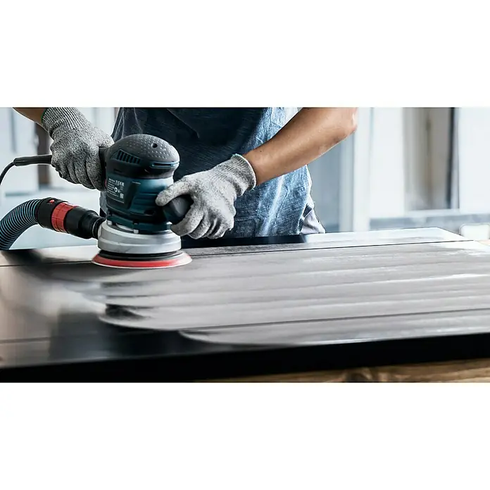 Bosch Expert Stützteller Multihole - 150 mm, Gelocht, Passend für: Exzenterschleifer - Detailaufnahme eines Werkers, der eine Bosch Exzenterschleifmaschine zum Schleifen einer Oberfläche mit Absaugung verwendet.