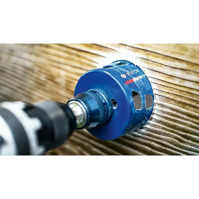 Bosch Professional Expert Bohrkrone Tough Material - Durchmesser Bohrer: 68 mm, 1 Stk. - Nahaufnahme einer Lochsäge der Marke Bosch, die in ein Holzbrett bohrt. Die blaue Lochsäge ist an einer Bohrmaschine befestigt.