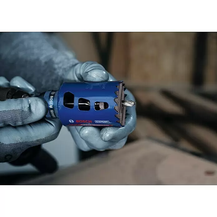 Bosch Professional Expert Bohrkrone Tough Material - Durchmesser Bohrer: 68 mm, 1 Stk. - Behandschuhte Hände halten eine blaue Bosch Expert Carbide Technology Lochsäge mit Zentrierbohrer, an einer Bohrmaschine befestigt.