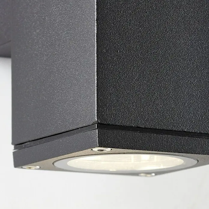 Brilliant Außenwandleuchte Hally - 60 W, 9,3 x 6,3 x 15,5 cm, Anthrazit, IP44 - Nahaufnahme einer modernen, würfelförmigen Außenleuchte in Schwarz, die ein warmes, einladendes Licht ausstrahlt.