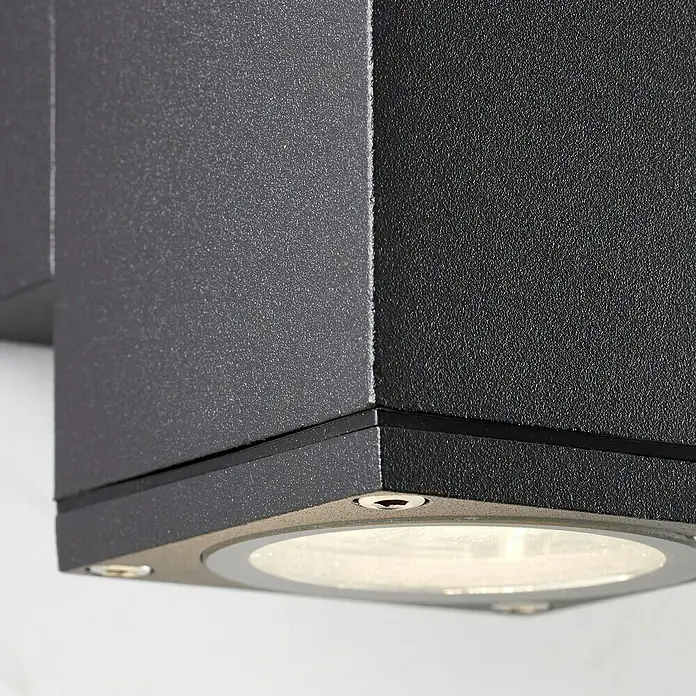 Brilliant Außenwandleuchte Hally - 40 W, 9,3 x 6,3 x 10,8 cm, Anthrazit, IP44 - Nahaufnahme einer modernen, würfelförmigen Wandleuchte in Schwarz, die ein helles, nach unten gerichtetes Licht ausstrahlt.