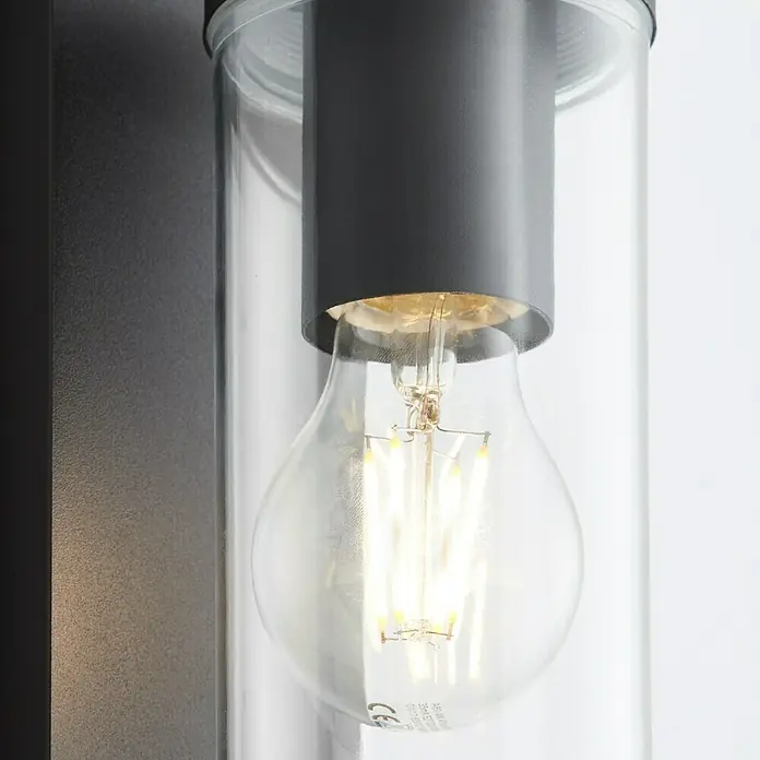 Brilliant Außenwandleuchte Aosta - 60 W, 12 x 8,5 x 30,6 cm, Schwarz matt, IP44, Hängend - Nahaufnahme einer modernen Wandleuchte mit einer klaren Glasröhre und einer Edison-Glühbirne, die ein warmes Licht ausstrahlt.