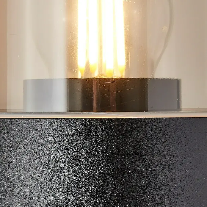 Brilliant Außenwandleuchte Sergioro - 40 W, 12,5 x 9 x 20,2 cm, Schwarz matt, IP44 - Nahaufnahme einer Tischleuchte mit einem klaren Lampenschirm, einem modernen Design und einem warmen Licht.
