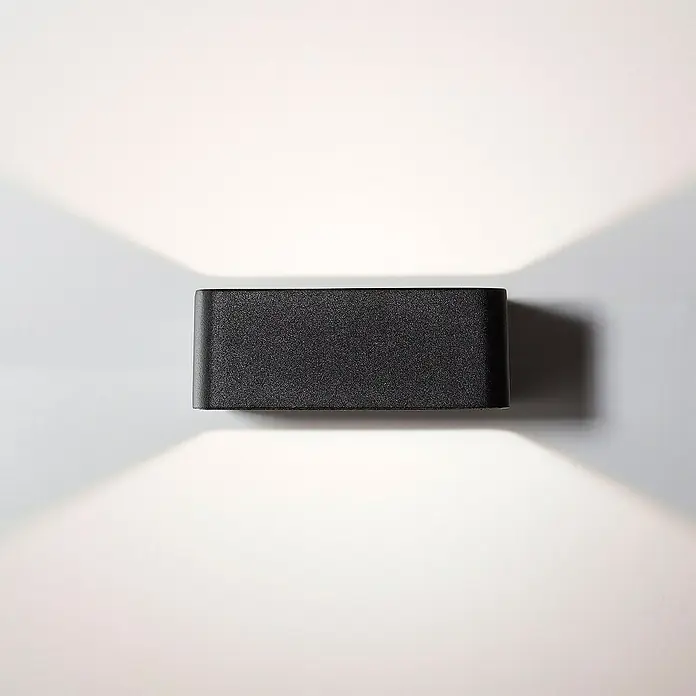 Brilliant LED-Außenwandleuchte Golda - 7 W, 14,5 x 12 x 4,5 cm, Schwarz, IP54 - Nahaufnahme einer stilvollen schwarzen Wandleuchte, die ein helles, warmes Licht nach oben und unten abstrahlt und eine moderne Ästhetik erzeugt.