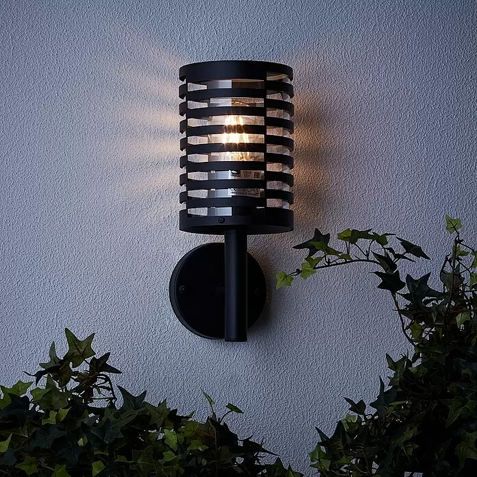 Brilliant Venlo Außenwandleuchte - 40 W, Ø x H: 12,7 x 30,5 cm, Schwarz matt, IP44 - Schwarze Außenwandleuchte mit Gitterdesign und warmem Licht, an texturierter Wand neben Efeupflanzen montiert.