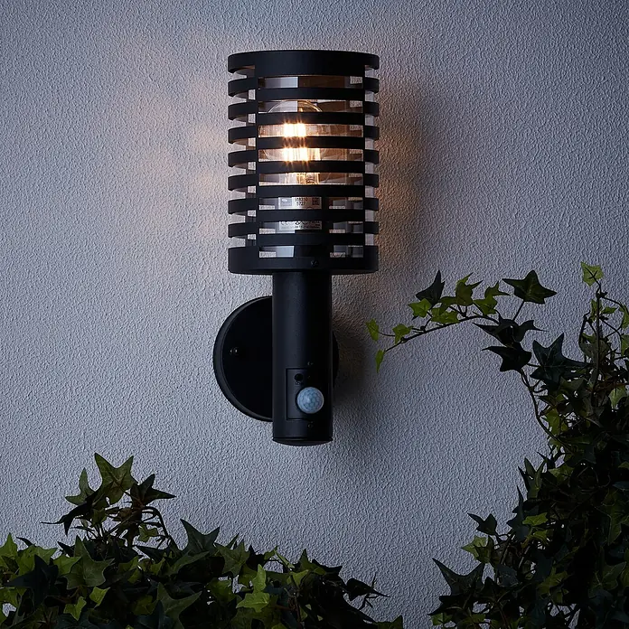 Brilliant Venlo Sensor-Außenleuchte - 18 W, Ø x H: 12,7 x 32,7 cm, Schwarz matt, IP44 - Eine elegante schwarze Wandleuchte mit Bewegungsmelder und einem dekorativen Gitter, das warmes Licht ausstrahlt und für Sicherheit sorgt.