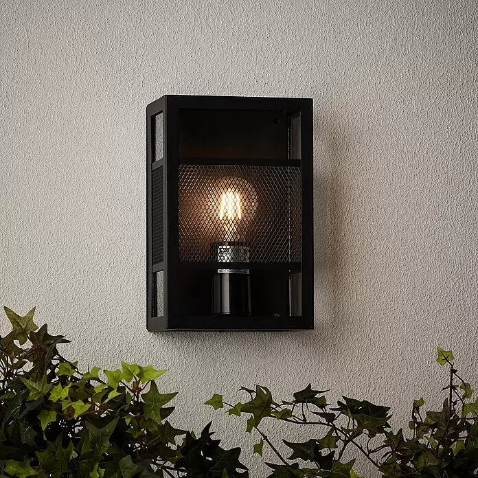 Brilliant Getta Außenwandleuchte - 20 W, 10 x 17 x 26 cm, Schwarz, IP44 - Schwarze industrielle Metall-Außenwandleuchte mit leuchtender Glühbirne, an strukturierter Wand mit Efeu montiert.