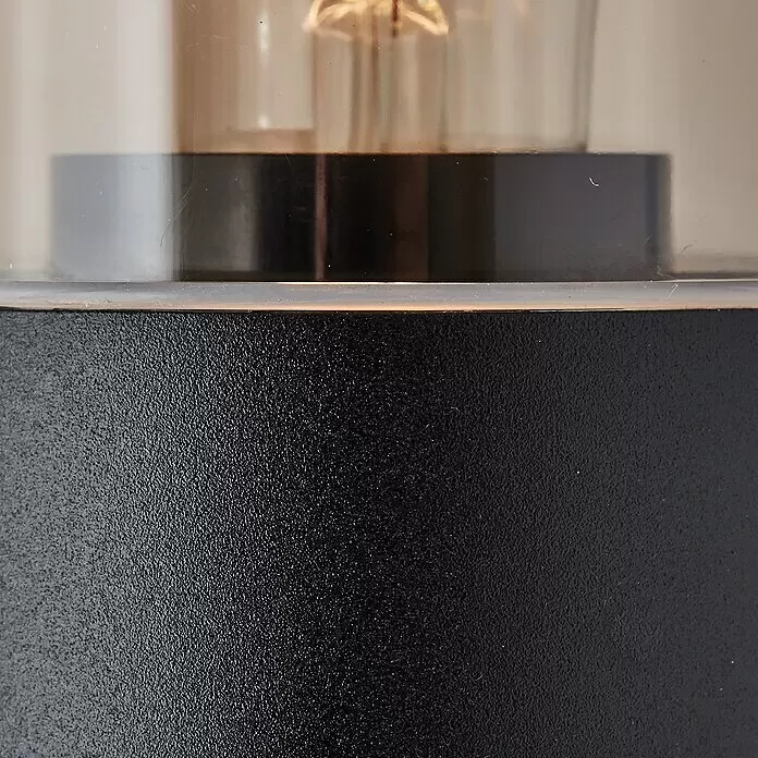 Brilliant Sensor-Außenleuchte Sergioro - 20 W, 12,5 x 9 x 20,2 cm, Schwarz matt, IP44 - Leuchte mit schwarzem strukturiertem Sockel und klarem zylindrischem Aufsatz, Glühbirne sichtbar.