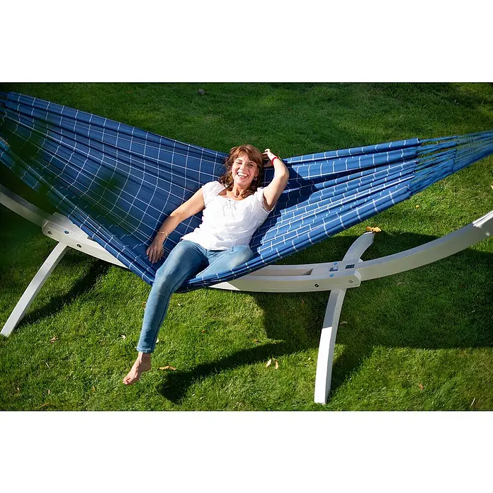 La Siesta Hängematte Brisa Kingsize - L x B: 400 x 180 cm, Marine - Eine Frau entspannt in einer blauen Hängematte mit weißen Karos, die auf einem weißen Gestell im grünen Gras steht.