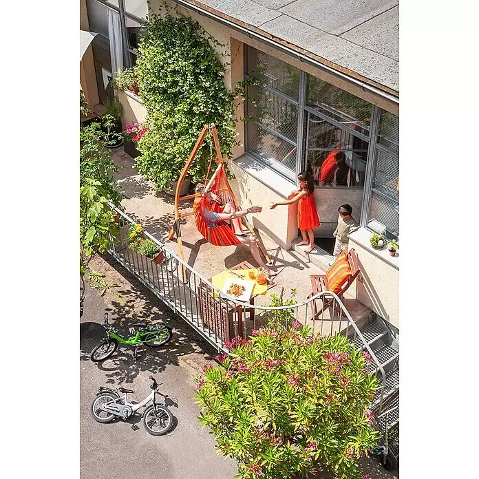 La Siesta Hängesessel Domingo Basic - Toucan - Mann entspannt in einem farbenfrohen gestreiften Hängesessel auf einem Holzgestell auf einer Außenterrasse.