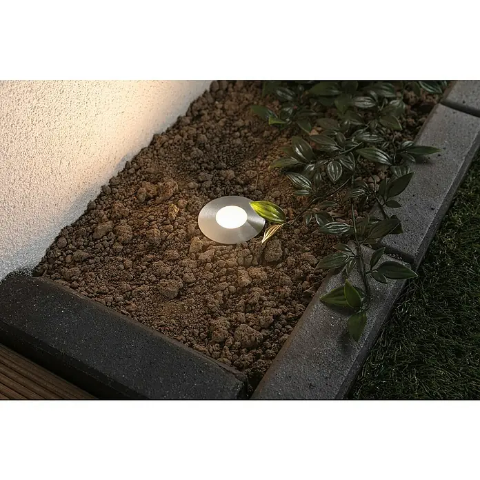 Paulmann Plug & Shine LED-Gartenspot Floor Mini - 2,5 W, 24 V, IP65 - Außenaufnahme einer runden, flachen Bodeneinbauleuchte in einem Beet, die ein warmes, gerichtetes Licht spendet.